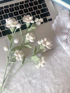 a laptop computer sitting on top of a white bed next to a bouquet of flowers