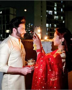 a man and woman standing next to each other holding candles in their hands while looking at each other