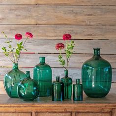 green vases with red flowers in them sitting on a wooden table next to each other