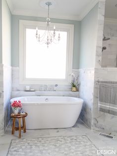 a white bath tub sitting under a window next to a wooden stool and sink in a bathroom