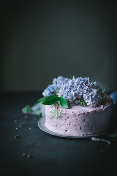 a cake with purple frosting and blue flowers on top is sitting on a plate