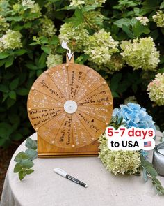 a wooden spinning wheel on top of a table next to some flowers and a pen