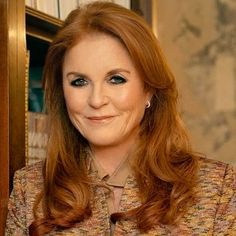 a woman with long red hair and blue eyes smiles at the camera while standing in front of a bookshelf