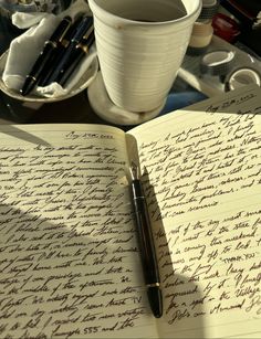 an open notebook with writing on it next to a coffee cup and other office supplies