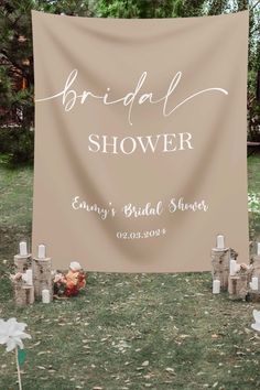 a bridal shower sign with candles and flowers on the ground in front of it