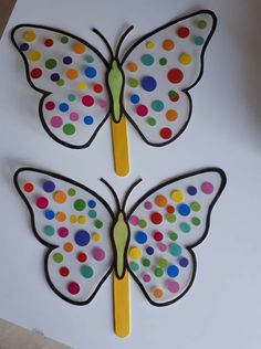 two butterflies made out of paper with colored dots on the wings and one has a toothpick in it