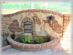 a brick wall with a door and flowers in the center is surrounded by plants, shrubs and rocks