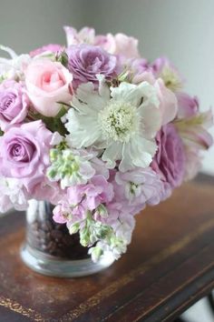 a vase filled with lots of purple and white flowers on top of a wooden table