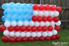 an american flag made out of balloons on the grass with a fence in the background