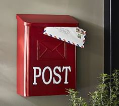 a red mailbox mounted to the side of a wall next to a potted plant