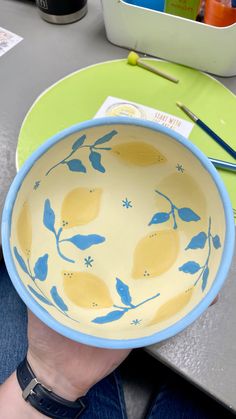 a hand holding a yellow and blue bowl with lemons painted on the side,