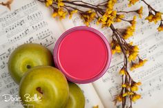 an apple and two green apples next to a pink paint container with yellow flowers on sheet music