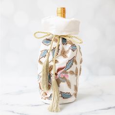 a bottle wrapped in fabric with a tasseled cap and gold top on a marble surface