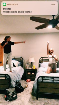 two people standing on top of twin beds in a room with ceiling fan above them