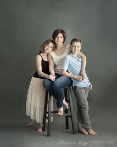 a woman and two children sitting on a stool in front of a gray background,