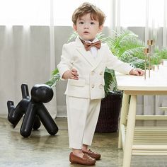 a little boy in a suit and bow tie standing next to a table with a balloon dog