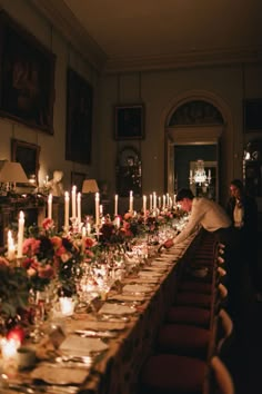 a long table with many candles and flowers on it in front of a man standing at the end