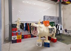 a sculpture of a white horse with its mouth open in front of clothes hanging on racks