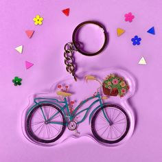 a keychain with a bicycle and flower pot on the front, against a purple background