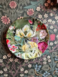 a plate with flowers painted on it sitting on a floral wallpapered tablecloth