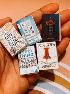 a person's hand holding several books in their palm, including one for john green and the other for john lewis