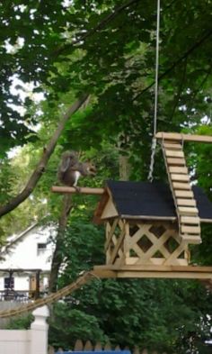 a squirrel sitting on top of a wooden bird house hanging from a wire above it