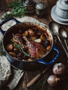 a pot filled with meat and potatoes on top of a wooden table next to garlic