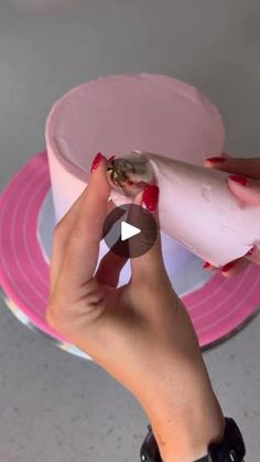 someone is decorating a cake with pink icing and white frosting on it