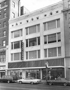 an old black and white photo of cars parked in front of a building on the street