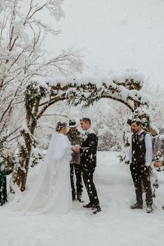 a bride and groom standing in the snow under an arch at their outdoor wedding ceremony