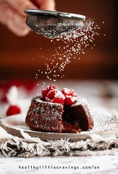 someone sprinkling sugar on some brownies with raspberries