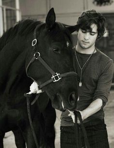 a black and white photo of a young man petting a horse