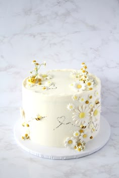 a white cake decorated with daisies on a marble countertop and topped with yellow flowers