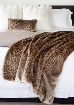 a leopard print blanket sitting on top of a white bed next to pillows and blankets