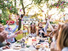 a group of people throwing confetti on each other at a table outdoors in the sun