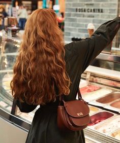 a woman with long red hair is standing in front of an ice cream display case