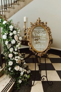 a welcome sign with flowers and a candle on a stand in front of a staircase