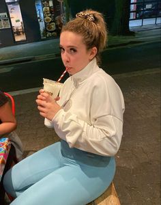 a woman sitting on a bench drinking from a cup with a straw in her mouth