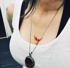 a woman wearing a white tank top and holding a brown necklace with a bird on it