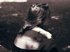 a woman with tattoos on her back sitting next to a bench and looking at the ground