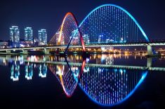 a bridge that is lit up in the night sky with lights on it and reflecting in the water