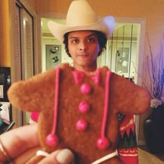 a man in a cowboy hat holding a fake gingerbread with pink icing on it