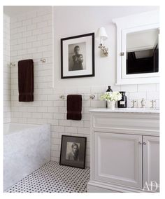 a white bathroom with black and white flooring, framed pictures on the wall above the bathtub