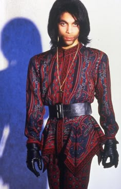 a man in a red and black outfit with long hair standing next to a white wall