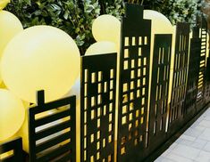 some yellow balloons are in the shape of city buildings and trees, along with black fence