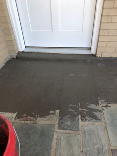 a white door is next to a red bucket and some bricks on the ground in front of it