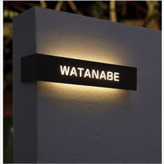 a white wall with a black sign that says wattanabe on the side