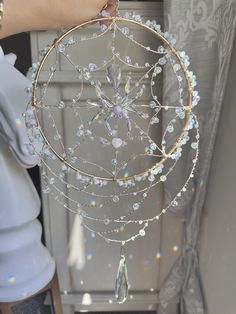 a person holding a gold and white beaded dream catcher