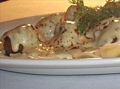 a white plate topped with ravioli covered in sauce and garnished with a sprig of rosemary