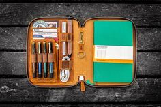 an open leather case with pens, scissors and other items inside on a wooden surface